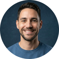 Smiling man with short dark hair and beard wearing a gray shirt against a dark blue background.